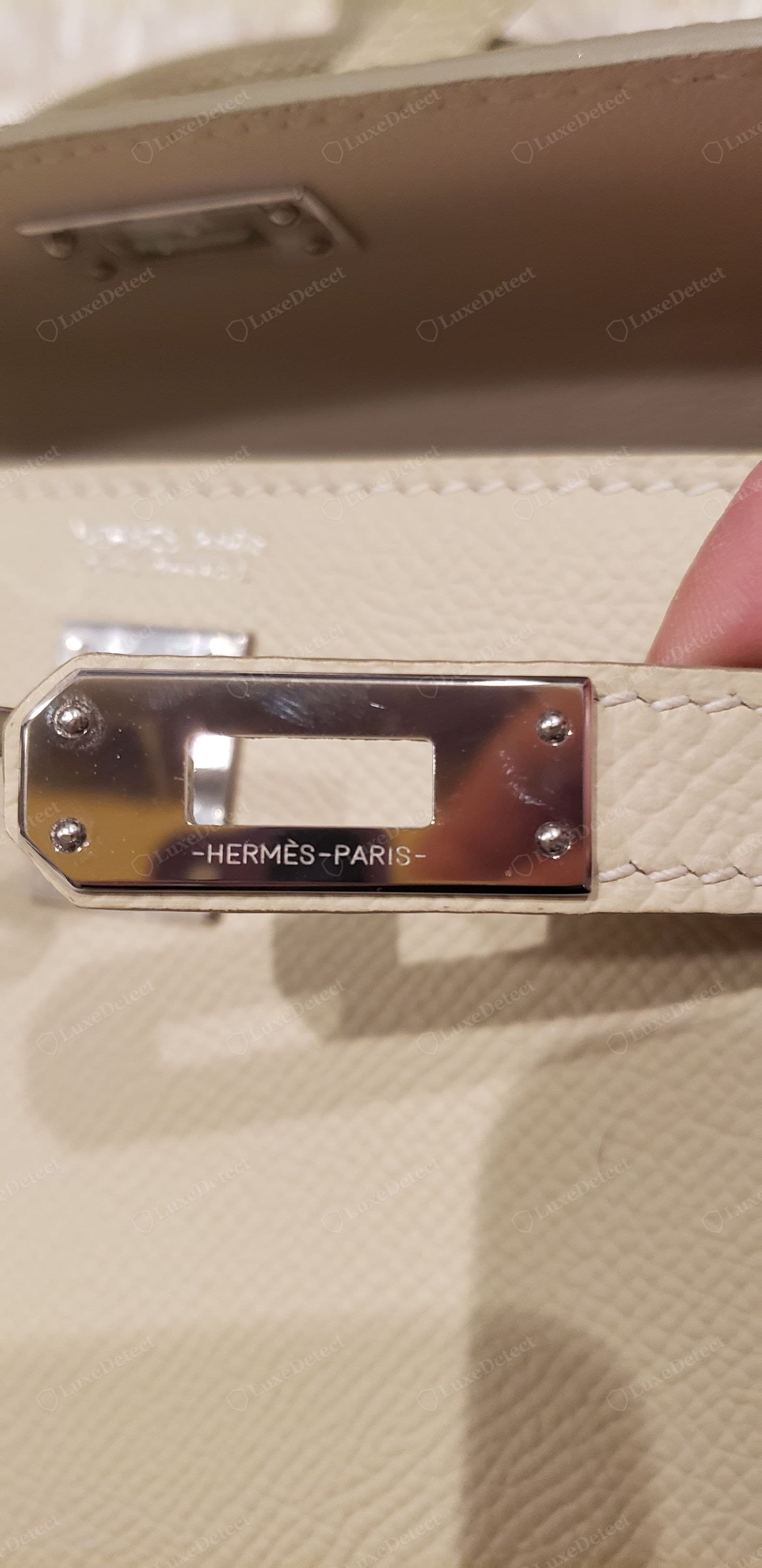 Counterfeit Hermès stitching — the "-HERMÈS-PARIS-" strap plate is etched shallow and slightly wobbly, and the seam above runs as a straight, uniform machine stitch with no hand slant