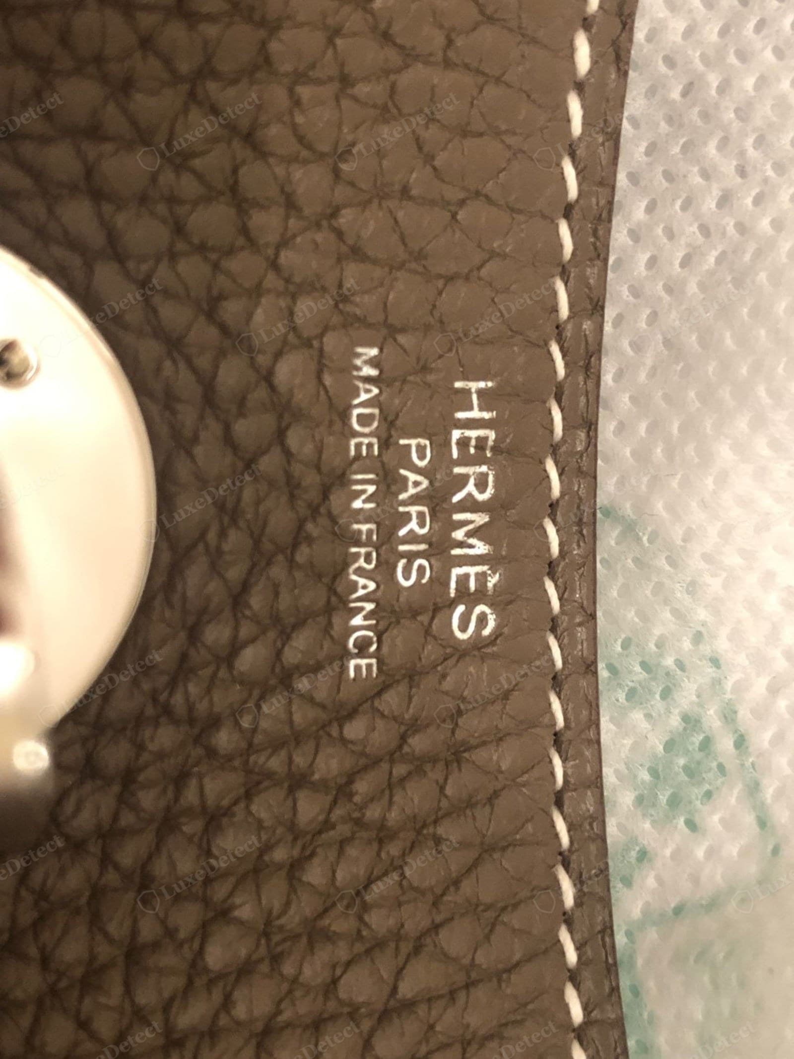 Genuine Hermès saddle stitching — a run of even, slightly slanted hand stitches in matte white waxed linen thread forming a neat diagonal-dash line beside the blind stamp on Étoupe grained calf