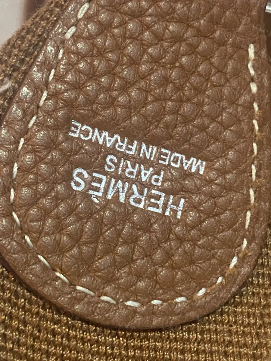 Blind stamp on a counterfeit Evelyne, tan strap keeper tab with a visibly heavier, less evenly spaced HERMÈS PARIS MADE IN FRANCE stamp