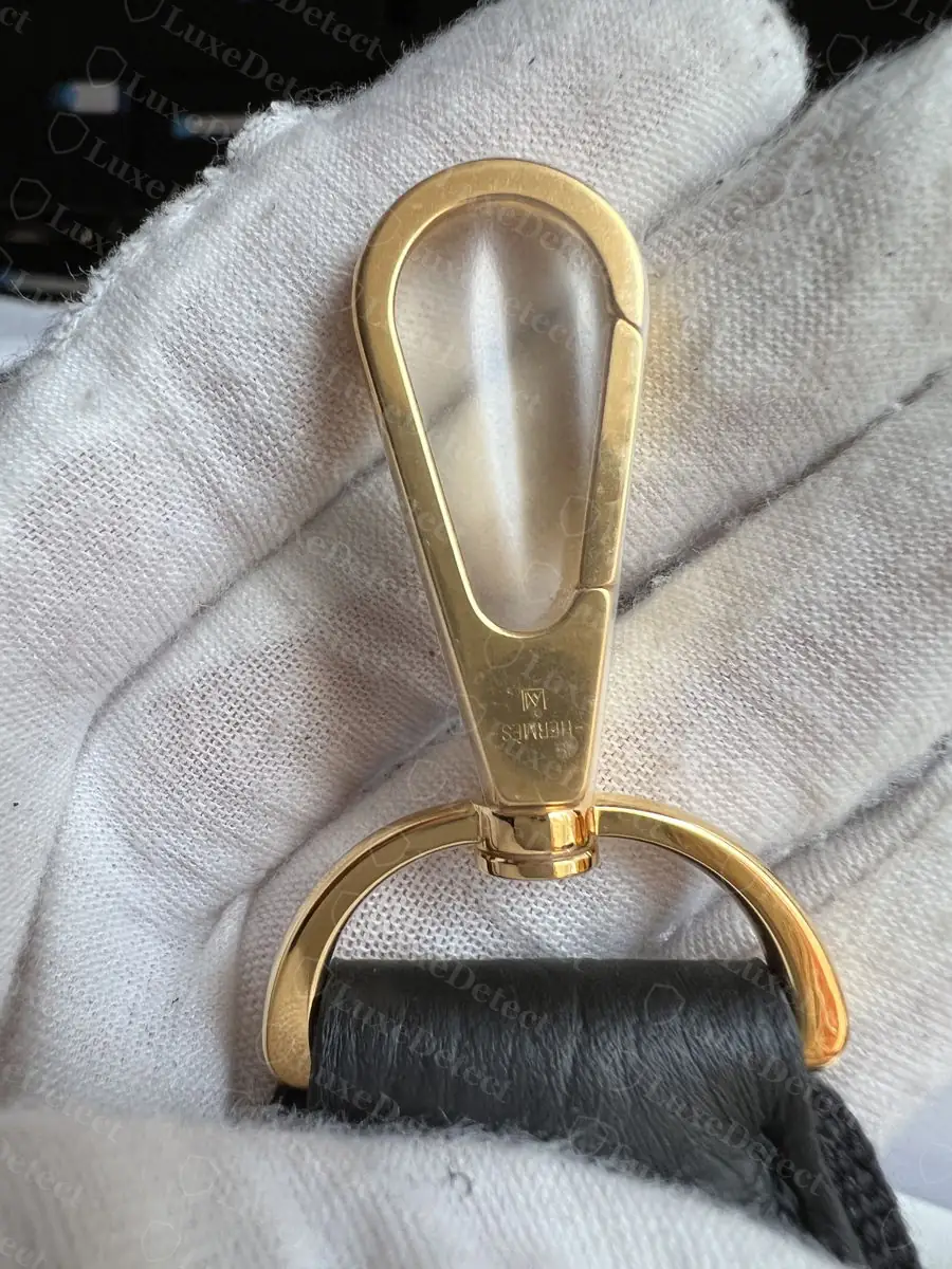 Genuine gold-hardware snap hook, HERMÈS engraved in crisp block letters on the flat face with a small maker's mark above the pivot