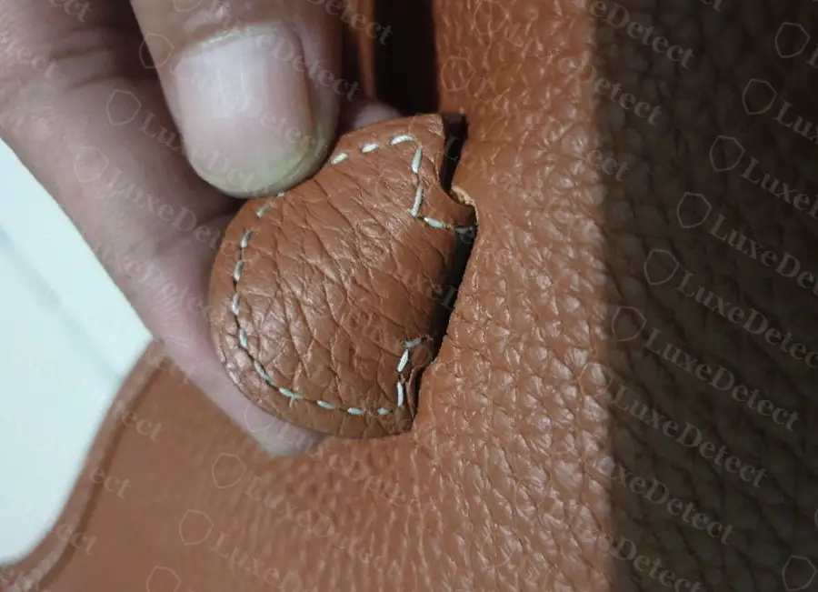 Strap keeper tab on a counterfeit Evelyne, stitching visibly running off the edge of the leather panel partway around the curve