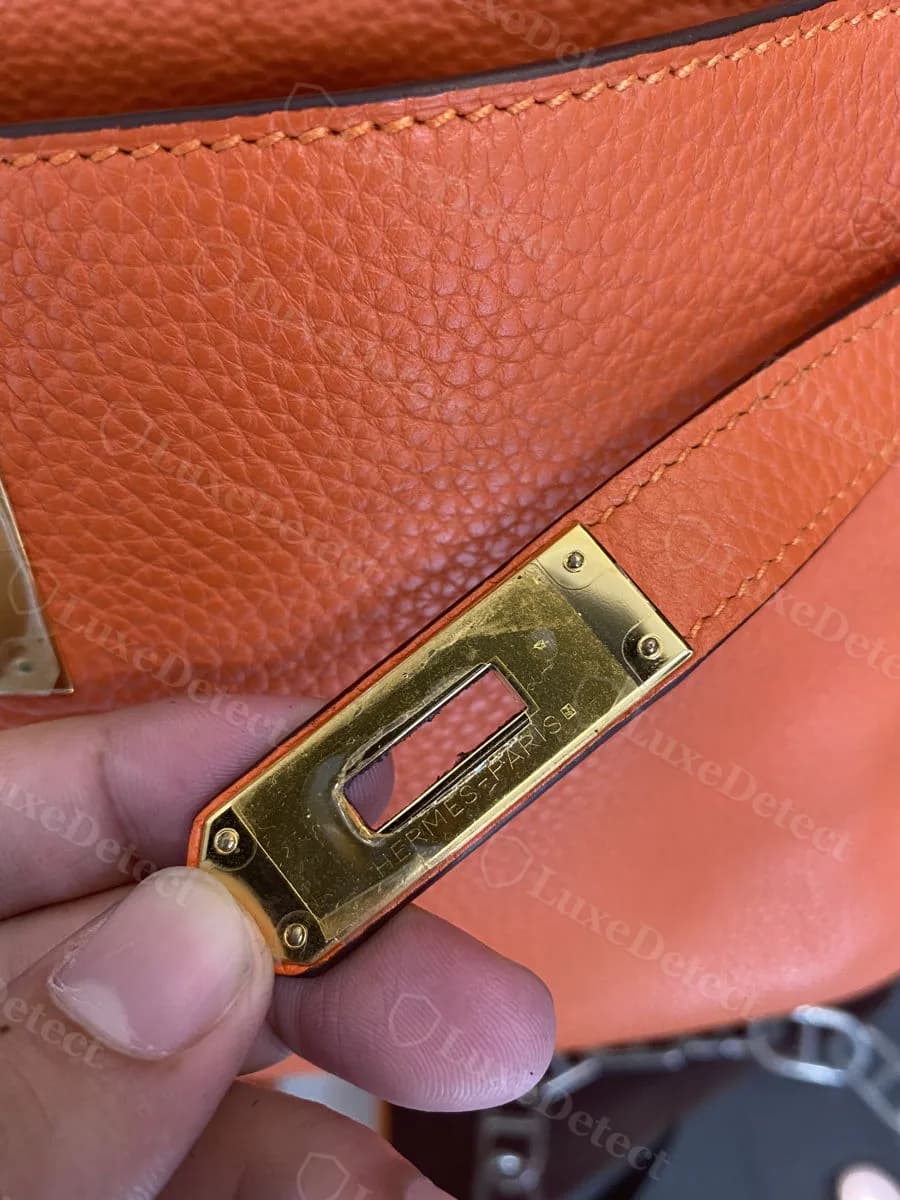 Genuine turn-lock plate on an orange Togo Kelly, HERMÈS-PARIS engraving clearly legible against the grain