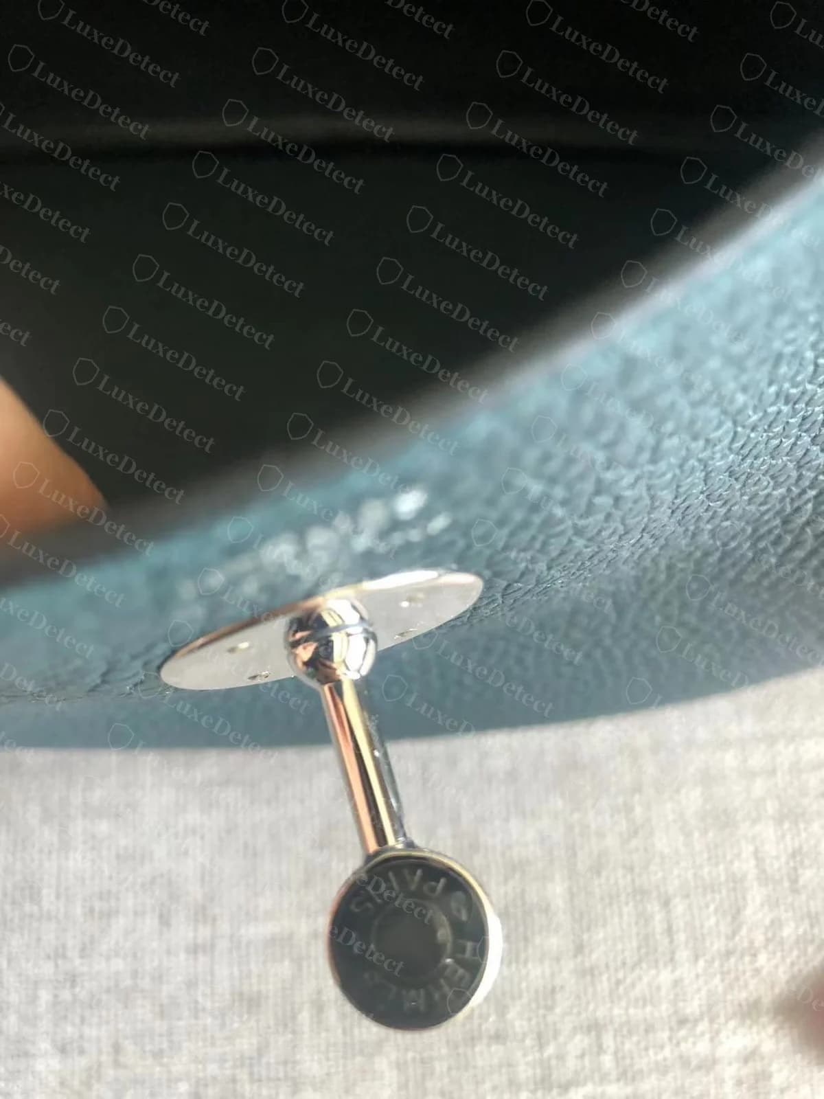 Genuine Hermès Lindy strap tab and rivet, teal Clemence leather, showing the rivet head stamped and centered in the reinforced leather tab