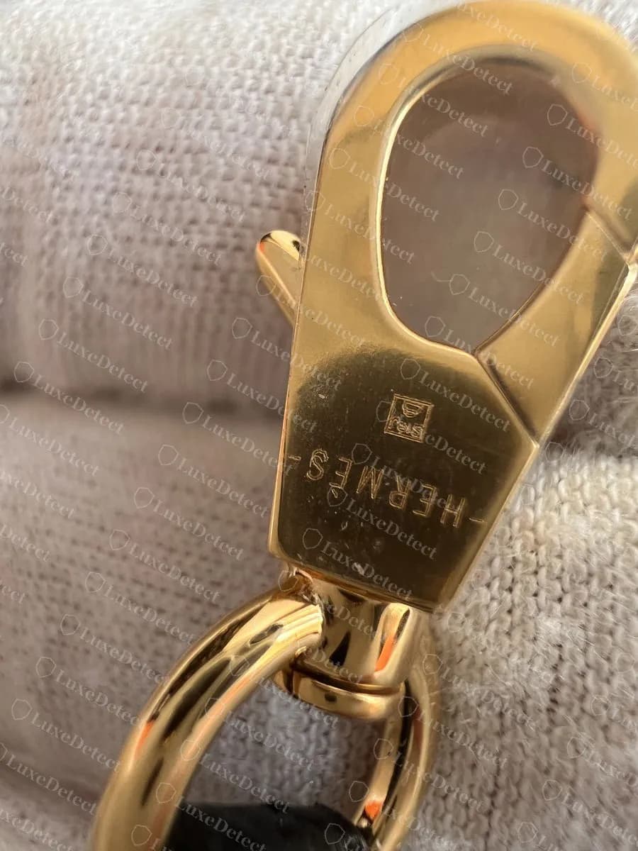 Genuine Mini Kelly II strap clasp in gold-tone hardware, HERMÈS engraved on the flat face beside a small square hallmark