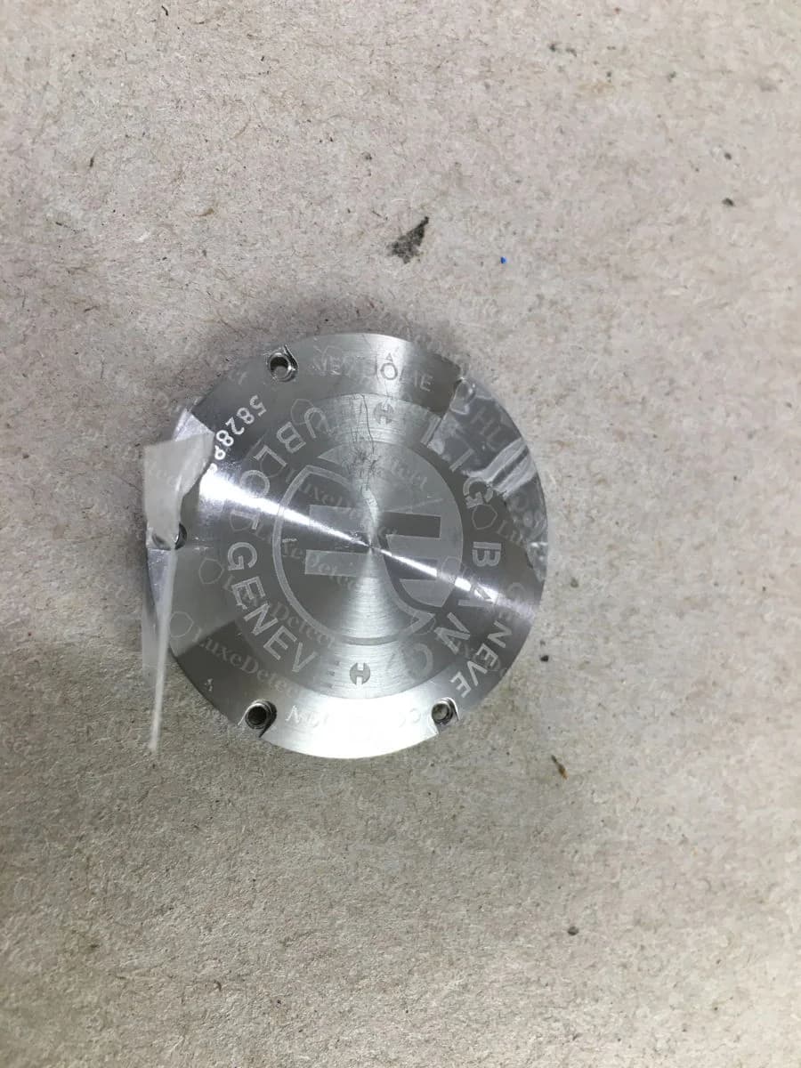 Counterfeit Hublot Big Bang caseback, removed from the watch — lightly etched "HUBLOT GENEVE BIG BANG" lettering around a large H, with a serial squeezed in at the edge