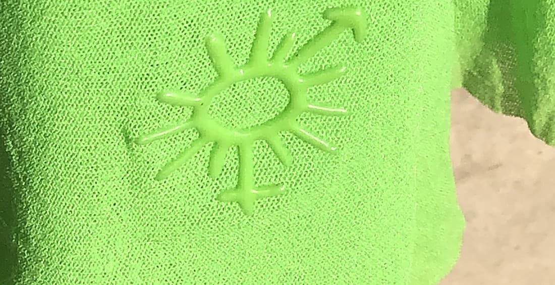 Genuine Jean Paul Gaultier cross-and-sun logo — a tonal, heat-pressed device on green knitwear, the same colour as the garment rather than a contrasting print