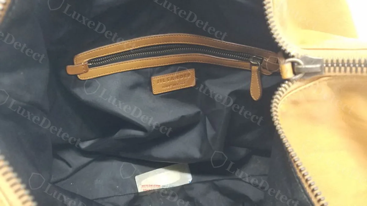 Authentic Jil Sander hobo bag interior, wide view showing the black fabric lining and stitched zip pocket with the leather brand tag visible