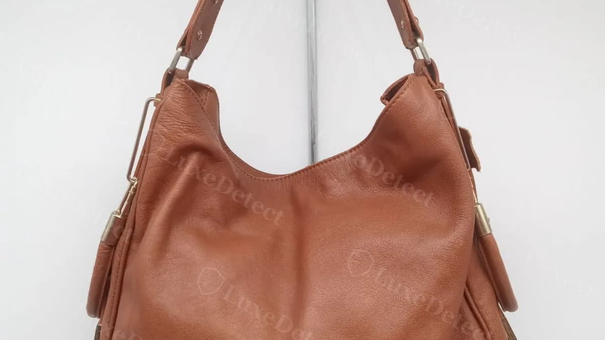 Full exterior silhouette of the confirmed fake Jil Sander hobo bag: pebbled cognac leather, gold-toned hardware bars, and an adjustable buckle strap