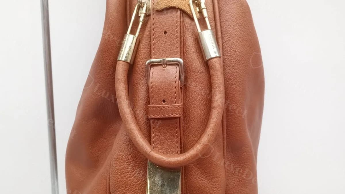 Confirmed fake Jil Sander hobo bag, hardware detail where the strap meets the body, showing "JIL SANDER" engraved as two words into the gold-toned hardware bar rather than debossed into the leather itself