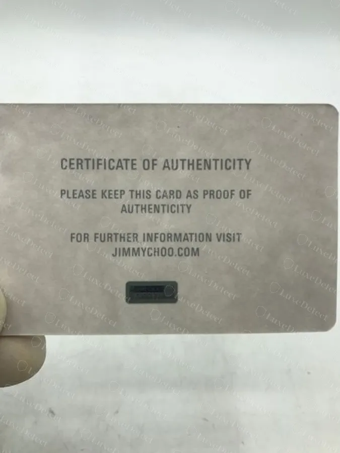Genuine grey Certificate of Authenticity card held in a hand, with a dark hologram panel and the jimmychoo.com wording