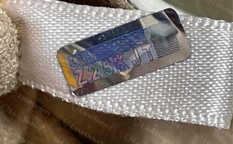 Genuine ribbon tag stitched inside a bag, with a hologram panel carrying an alphanumeric code in silver and blue lettering