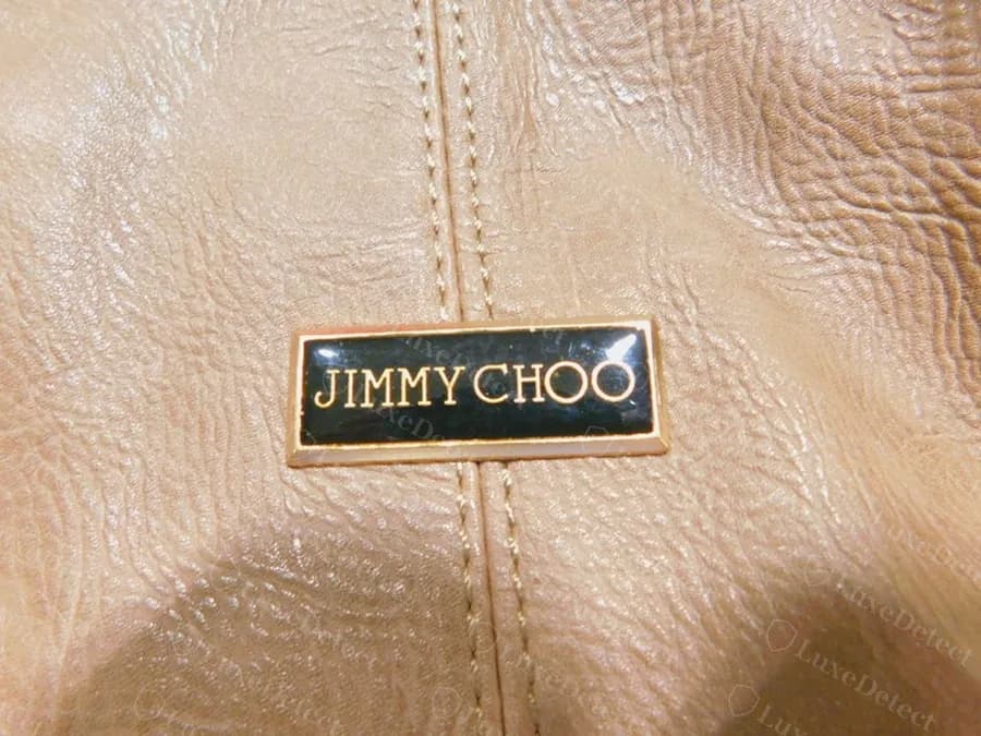 Counterfeit tan bag with a glossy domed black enamel plaque in a gold rim, gold capitals set tightly together, centred over the front seam