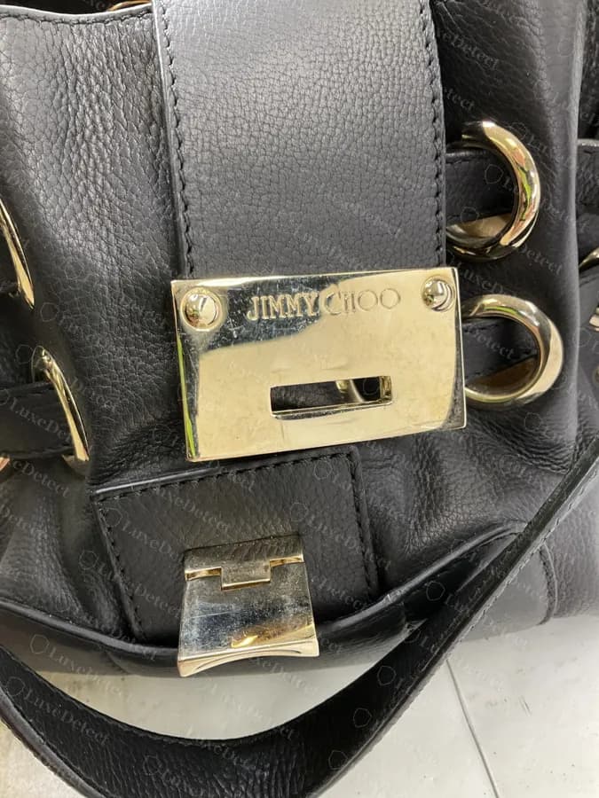 Placa de cierre genuina de un Ramona en metal dorado pulido con JIMMY CHOO grabado en la parte superior, sobre cuero negro granulado con un cierre giratorio dorado debajo