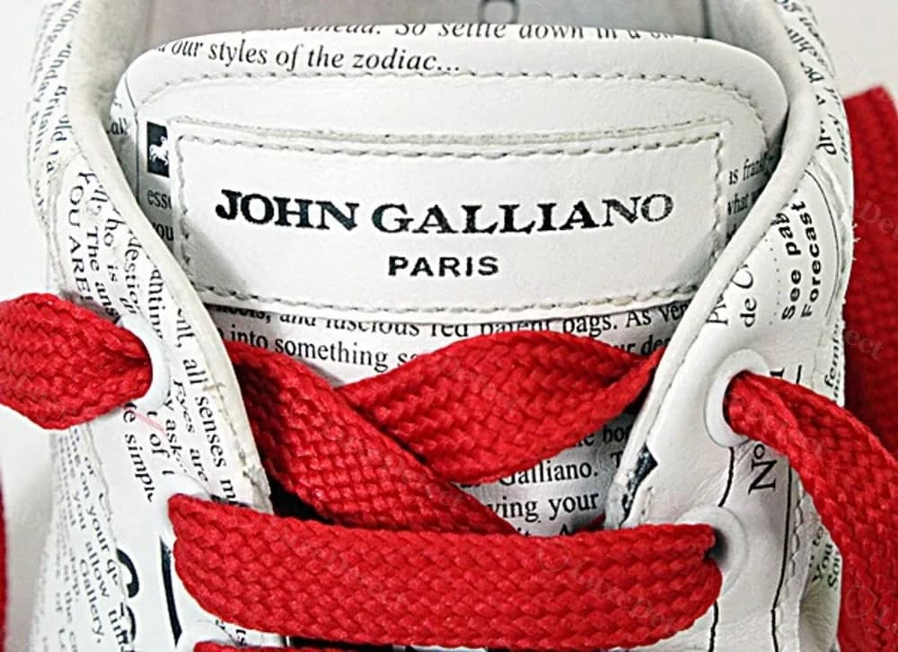 Authentic John Galliano Newsprint sneaker tongue tag, clean serif "JOHN GALLIANO PARIS" set inside a dedicated white label.