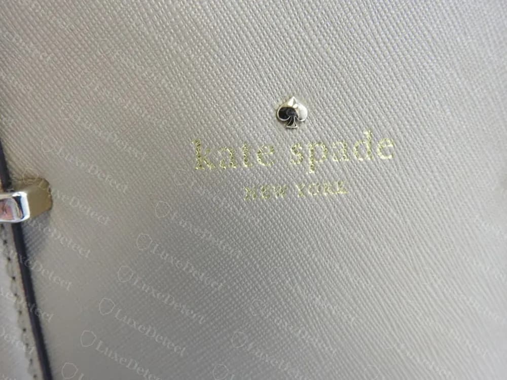Genuine Kate Spade blind-debossed spade icon and foil-stamped "kate spade NEW YORK" wordmark on cream leather, showing the pressed outline of the deboss beneath the gold foil lettering