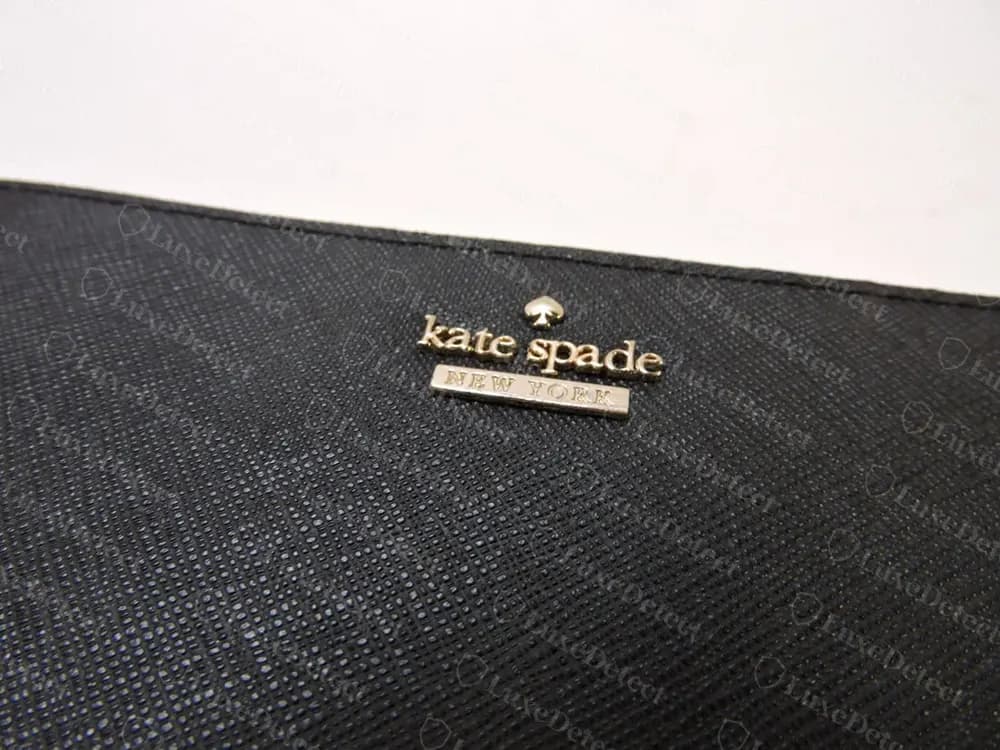 Genuine Kate Spade foil-stamped gold wordmark on black saffiano leather, with the spade icon centred above "kate spade" and "NEW YORK" set in a small rectangle beneath