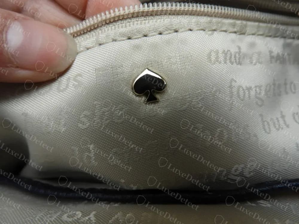 Genuine Kate Spade enamel-filled spade rivet set into printed lining fabric featuring literary-style text, a decorative hardware detail seen inside several current bags
