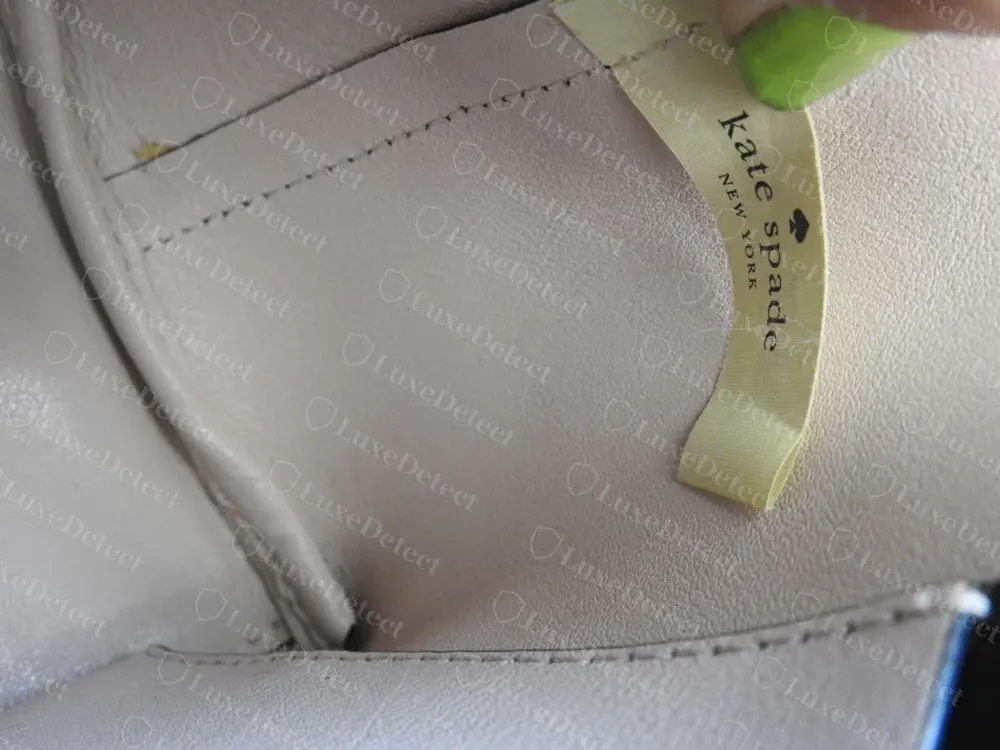 Genuine Kate Spade woven fabric interior tag sewn into a lining seam, reading "kate spade NEW YORK" with a small spade icon, on striped cotton lining