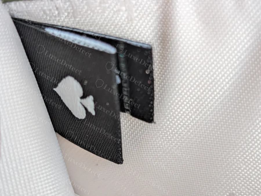 Genuine Kate Spade black woven interior tag with a white spade, partly tucked into a pocket seam of a pale lining