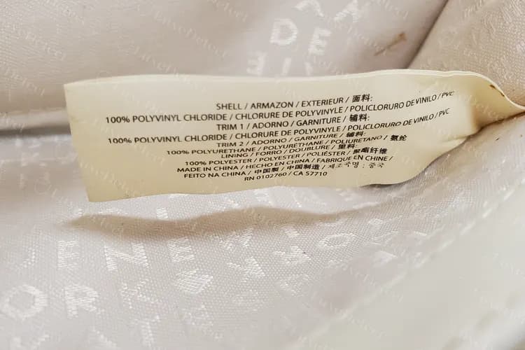 Etiqueta de cuidado genuina de Kate Spade cosida en el forro de una cartera, con la lista de PVC en el exterior y los acabados, poliuretano, forro de poliéster y un país de fabricación en varios idiomas