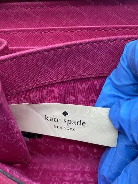 Etiqueta tecida creme original da Kate Spade com "kate spade NEW YORK" e um espade acima, sobre um forro rosa com letras repetidas impressas
