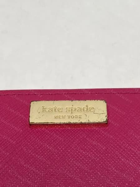 Genuine Kate Spade rectangular gold-tone metal plate engraved "kate spade NEW YORK" on pink saffiano leather, mounted flat with no visible rivets and showing light surface wear