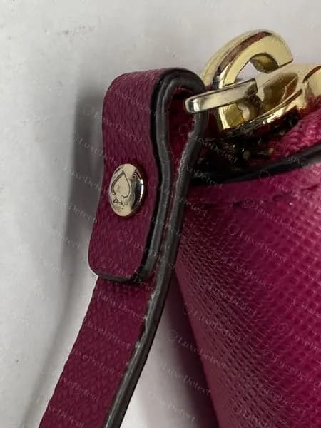 Genuine Kate Spade wristlet strap folded through a gold-tone ring, with a round gold-tone rivet engraved with a spade on the strap