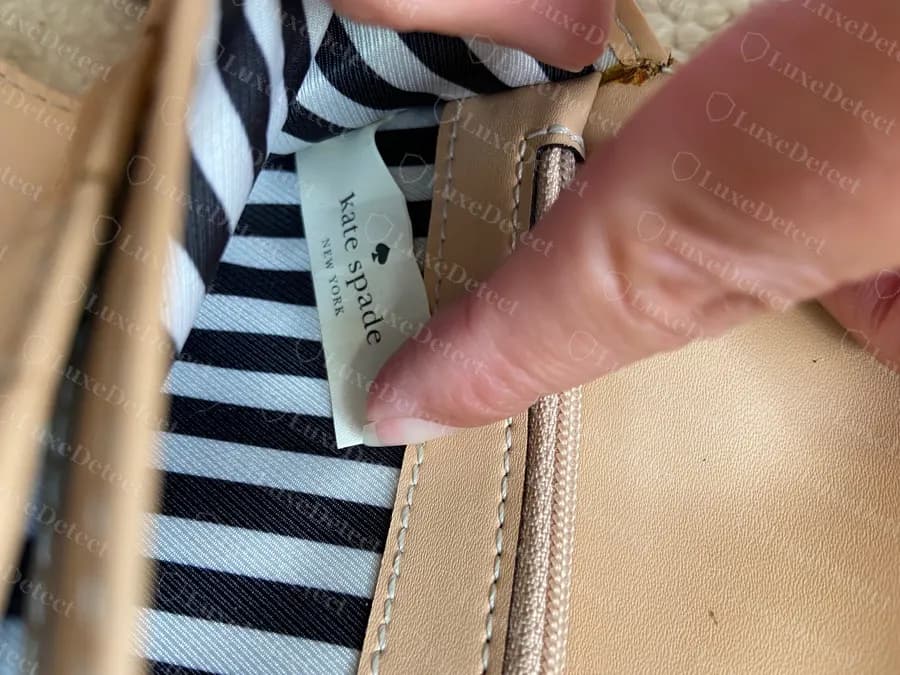 Interior de uma carteira Kate Spade original com forro de cetim listrado azul-marinho e branco, uma etiqueta tecida creme e uma seção de cartões em couro caramelo