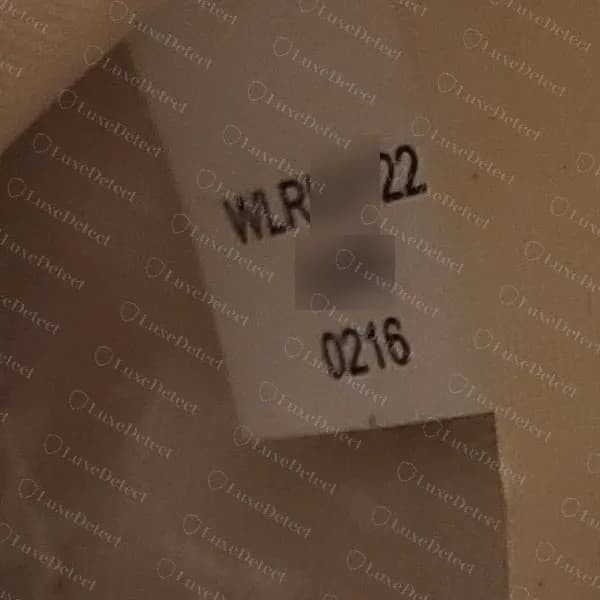 Genuine Kate Spade sewn style tag showing a style line starting W then LR, a blurred middle, a blurred factory-code line and a four-digit date line reading 0216