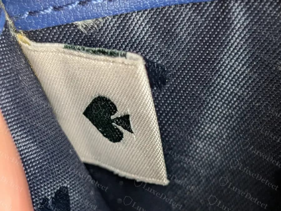 Genuine Kate Spade cream woven interior tag carrying only a dark spade, sewn into the seam of a navy lining