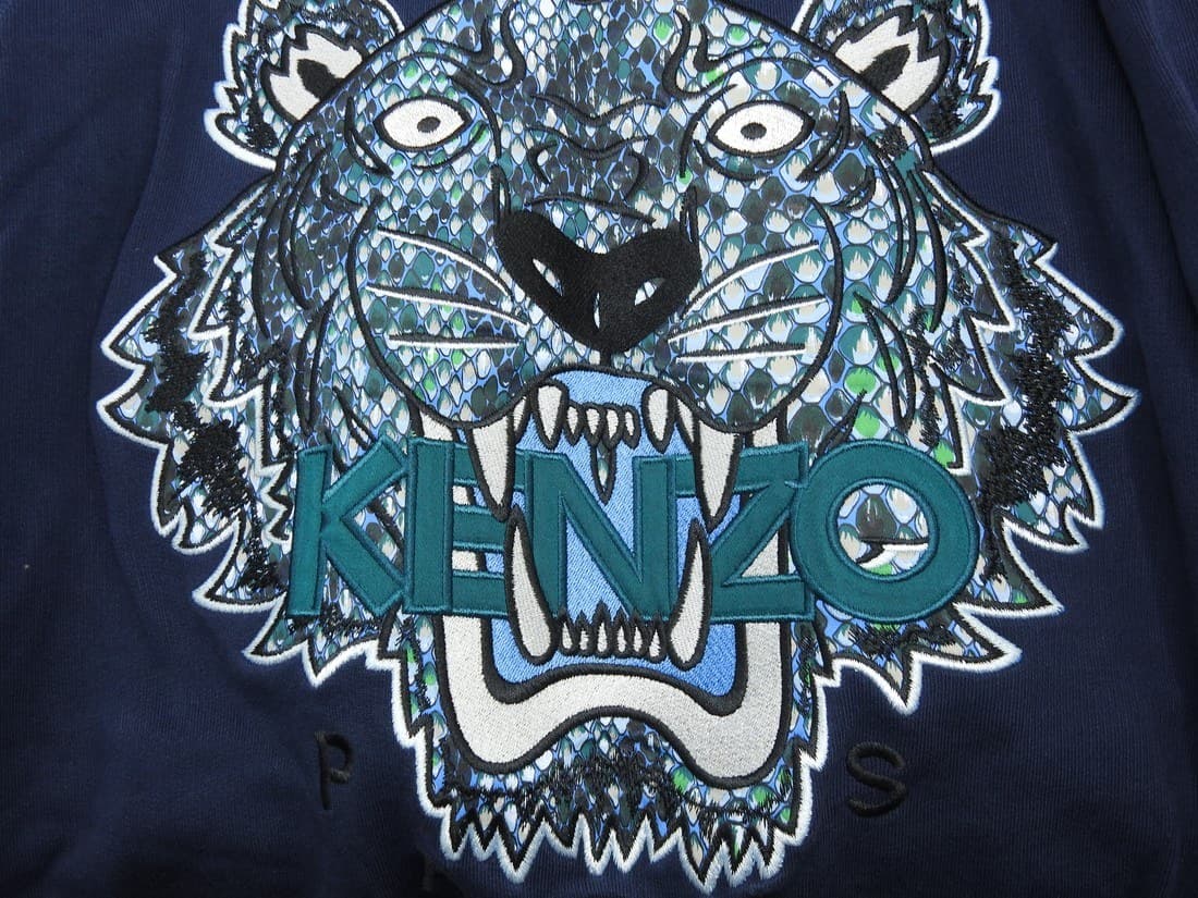 Counterfeit Kenzo Tiger embroidery — genuinely embroidered with real satin-stitch texture, but the face is filled with a busy, mottled, scale-like pattern instead of clean color-blocked panels