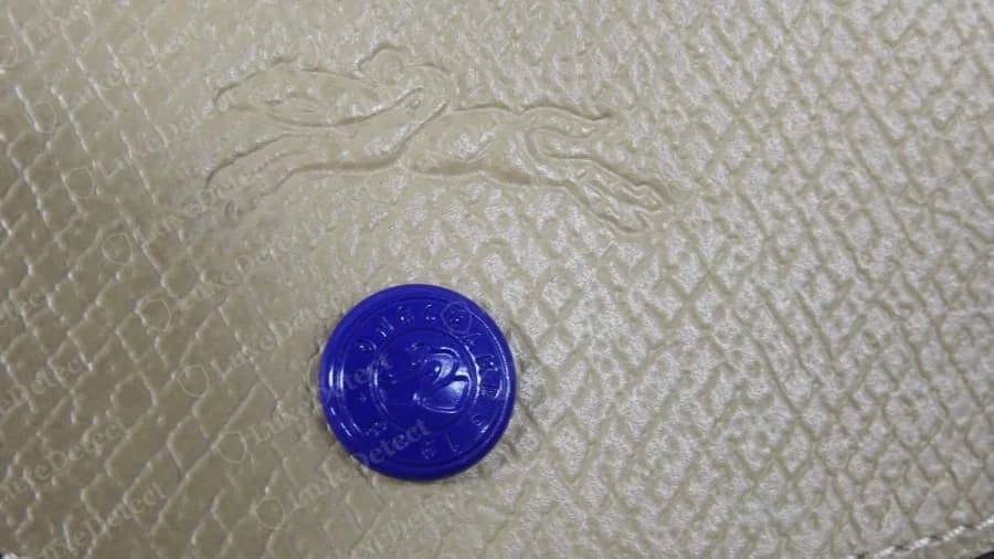 Variante Longchamp Le Pliage authentique avec un bouton-pression bleu coloré sur cuir beige et un cheval gaufré à blanc au-dessus