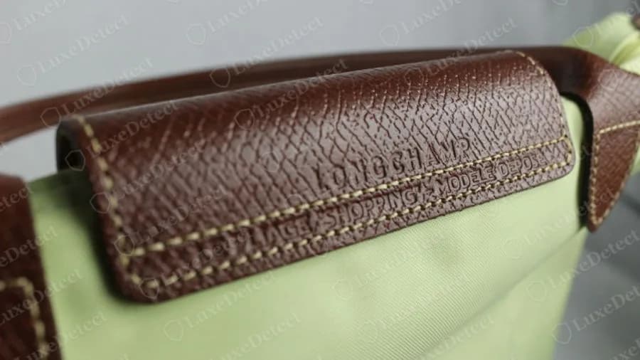 Borde de asa forrado de piel de Longchamp original, una tira de piel marrón cosida y sellada con LONGCHAMP con una segunda línea de texto sellado debajo, sobre un cuerpo de nailon verde claro