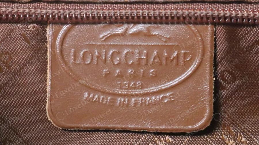 Etiqueta interior de un bolso de piel antiguo de Longchamp original, una etiqueta ovalada de piel sellada que dice LONGCHAMP PARIS 1948 MADE IN FRANCE, cosida en un forro con estampado de monograma