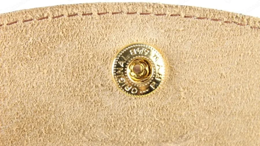 Broche de Longchamp original visto desde el interior de la solapa, un broche dorado sobre ante color arena sellado con ORIGINAL PRYM alrededor del borde