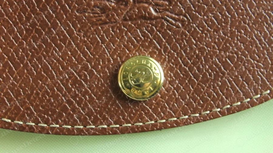 Echter goldener Longchamp-Druckknopf auf der Lederklappe, ein runder Knopf mit Pferdemonogramm und Schriftzug LONGCHAMP 1948 am Rand, auf feinem braunem Leder mit Kreuzschraffur-Narbung