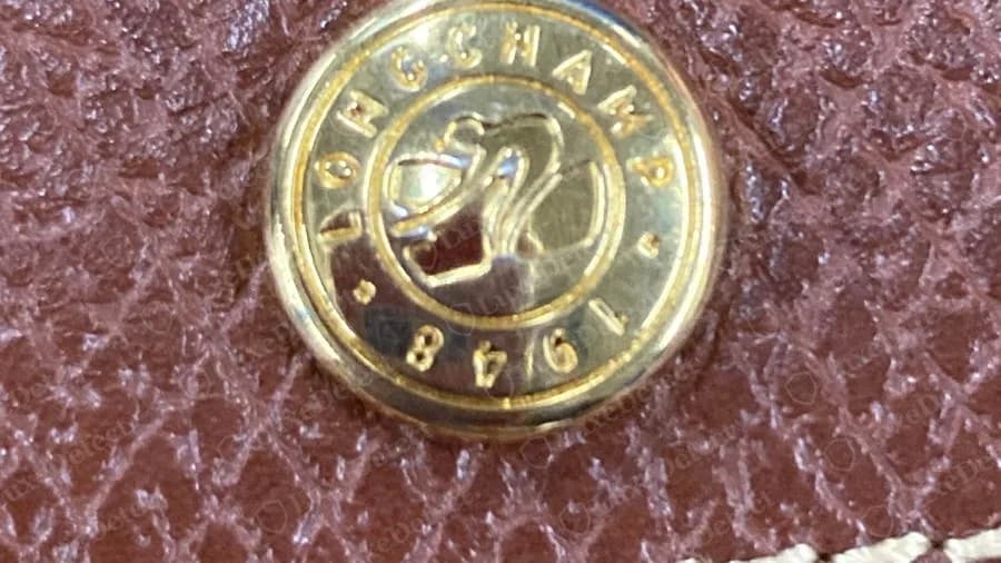 Gros plan sur la face d'un bouton-pression Longchamp authentique sur un cuir brun rosé, monogramme du cheval dans un cercle avec LONGCHAMP et 1948 sur le pourtour