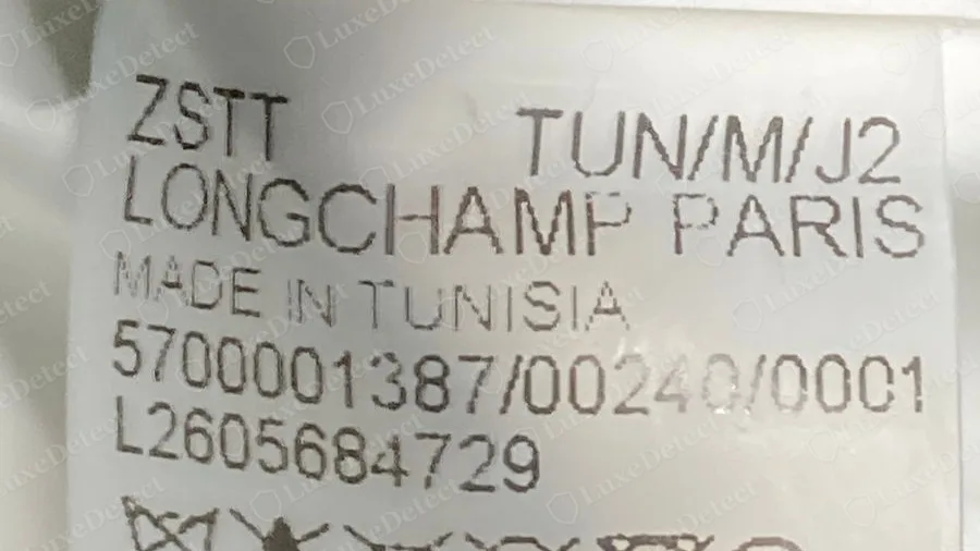 Etiqueta interior de Longchamp original de un bolso fabricado en Túnez, un código de cuatro letras, LONGCHAMP PARIS, MADE IN TUNISIA, una línea de producto más larga y un segundo código que empieza por L