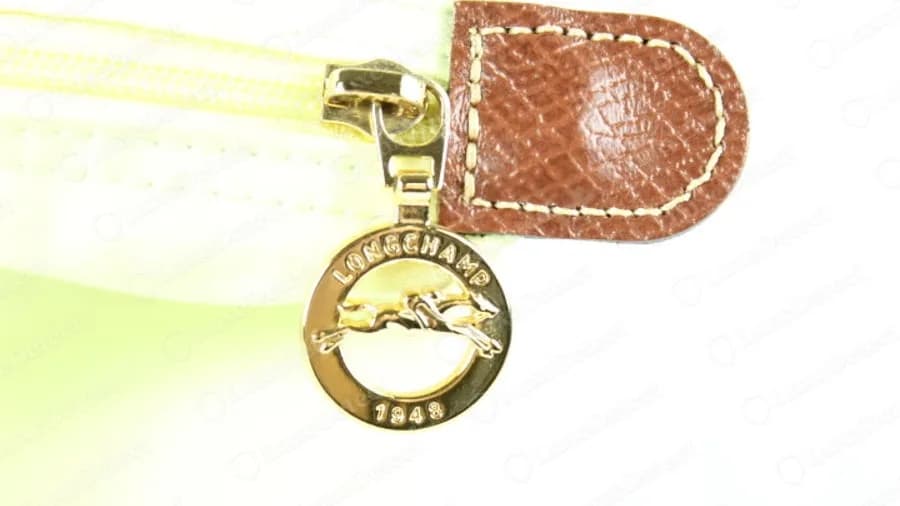 Genuine Longchamp zip pull in gold tone: an engraved ring with a horse and jockey, LONGCHAMP along the top and 1948 along the bottom, hanging from a leather tab