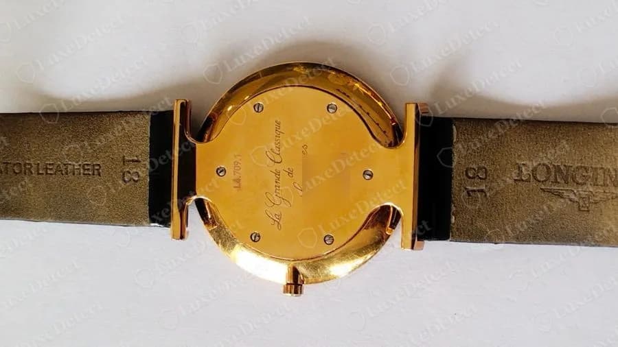 Genuine Longines La Grande Classique gold-tone caseback engraved La Grande Classique de, with a reference starting L4 on the left, four screws and a reference starting L4, photographed on a strap lined with LONGINES and a winged hourglass