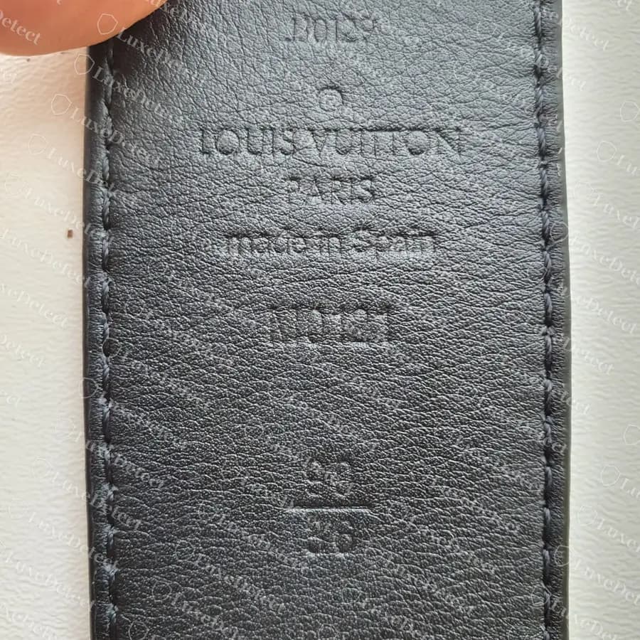 Genuine reversible Louis Vuitton Initiales strap tip: date code at the top, then the circle R, LOUIS VUITTON PARIS made in Spain, the M model number and a 90 over 36 size, all in thin, evenly spaced letters