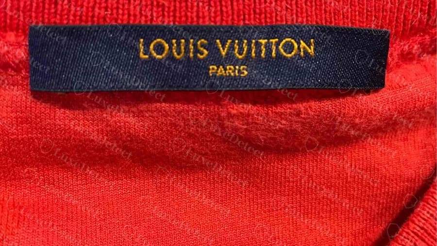Etichetta del collo originale di una maglietta Louis Vuitton: etichetta tessuta blu navy con LOUIS VUITTON sopra PARIS in maiuscole dorate, su una maglietta rossa