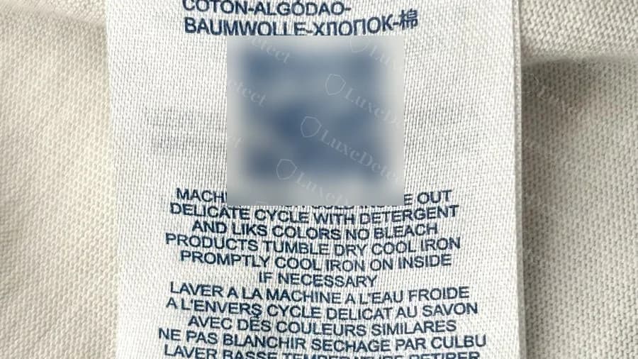 Counterfeit white care label on a different tee, with a large QR code (blurred), multilingual care text and Made in FRANCE