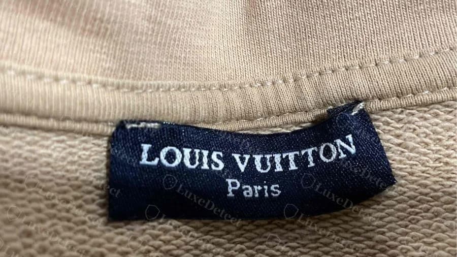 Counterfeit Louis Vuitton hoodie neck label in white serif lettering with Paris in mixed case, unlike the genuine gold capitals