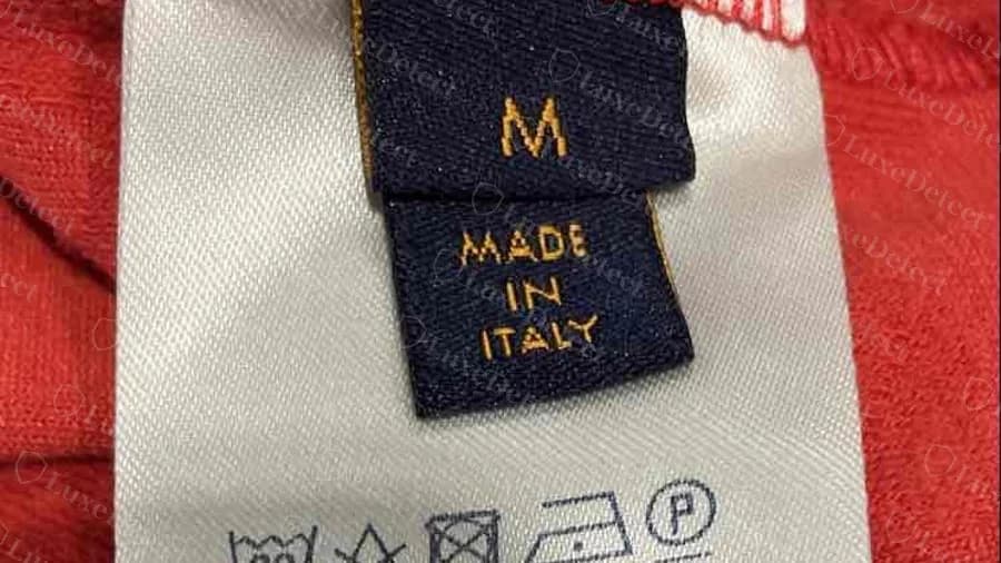 Étiquette de taille M d'un t-shirt Louis Vuitton authentique au-dessus d'une étiquette bleu marine MADE IN ITALY, cousue à une étiquette d'entretien en satin blanc avec symboles d'entretien