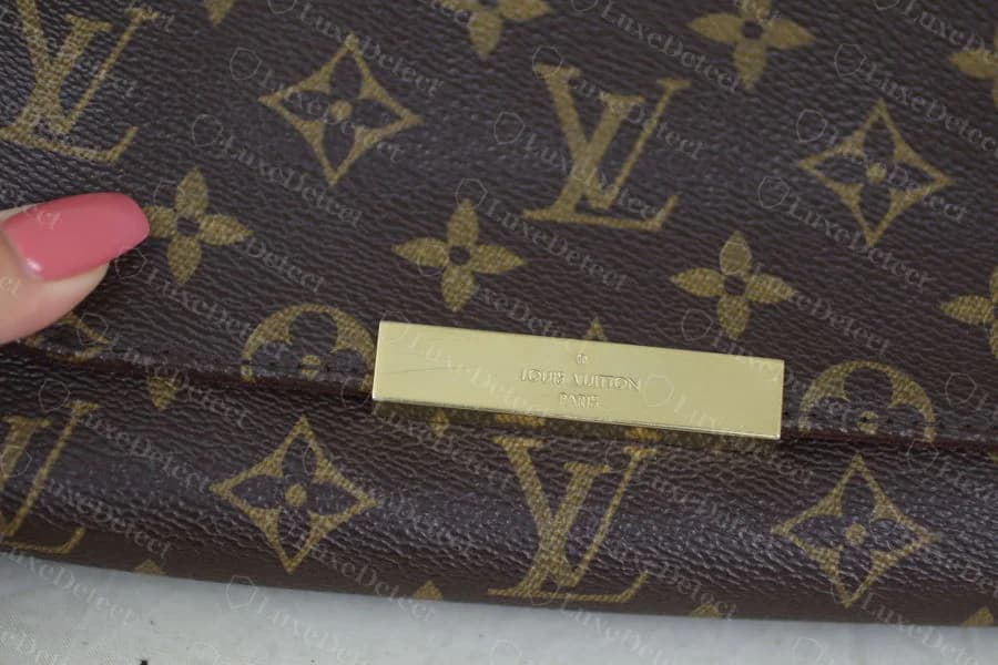 Close detail of the genuine gold plaque on Monogram canvas, warm gold tone, evenly struck wordmark, centered registration mark above LOUIS VUITTON