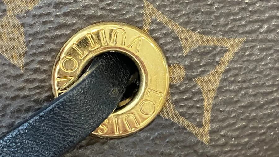 Genuine Neonoe grommet: a polished brass ring reading LOUIS VUITTON around the edge, with the black leather drawstring running through it