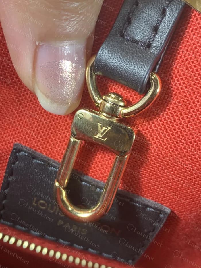 Authentic swivel clasp on a Louis Vuitton OnTheGo, with a crisp centered LV stamp and a visible rivet detail beside it