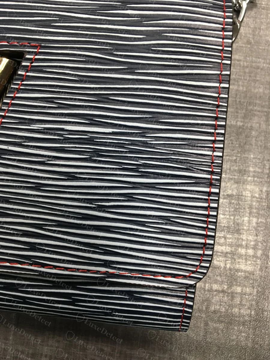 A counterfeit Twist clasp from our archive on a printed zebra-pattern flap — the clasp sits off-center in its cutout with an uneven gap, and the exposed red stitching outline is a further tell covered in the leather check below