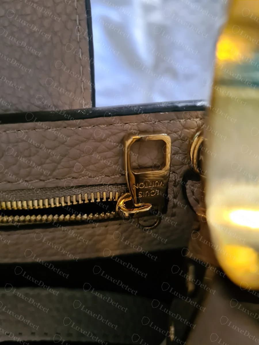 Genuine Capucines interior zipper pull, engraved "LOUIS VUITTON" in a clean, evenly struck sans-serif font